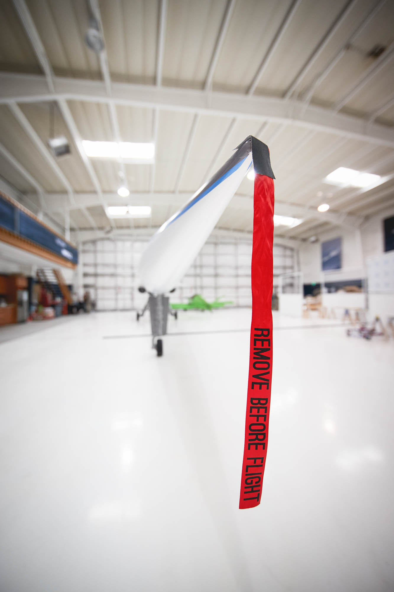 Close-up of a pitot tube cover with a red Remove Before Flight streamer attached to the nose of the Boom XB-1 supersonic prototype in a hangar