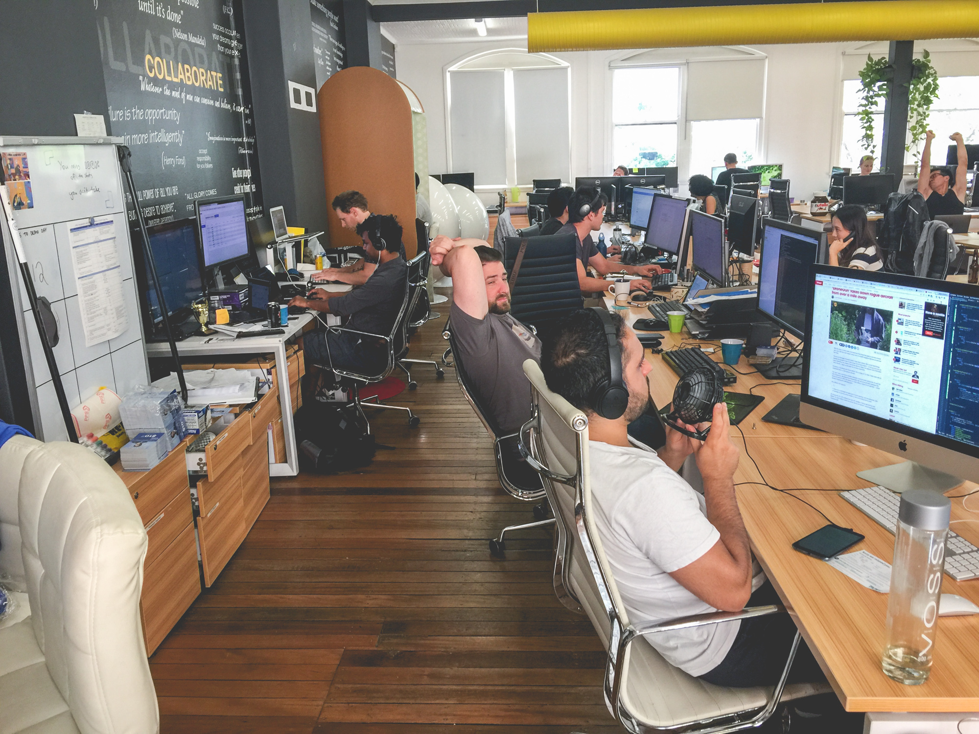 Snappr team working at long shared desks with iMacs and dual monitors in their Sydney office