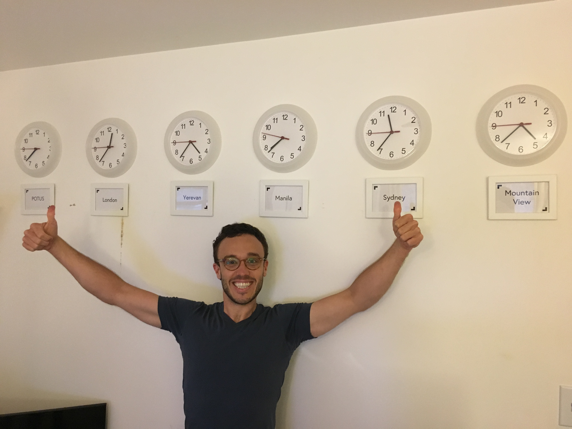 Snappr team member giving thumbs up under row of world clocks showing POTUS, London, Yerevan, Manila, Sydney, Mountain View time zones
