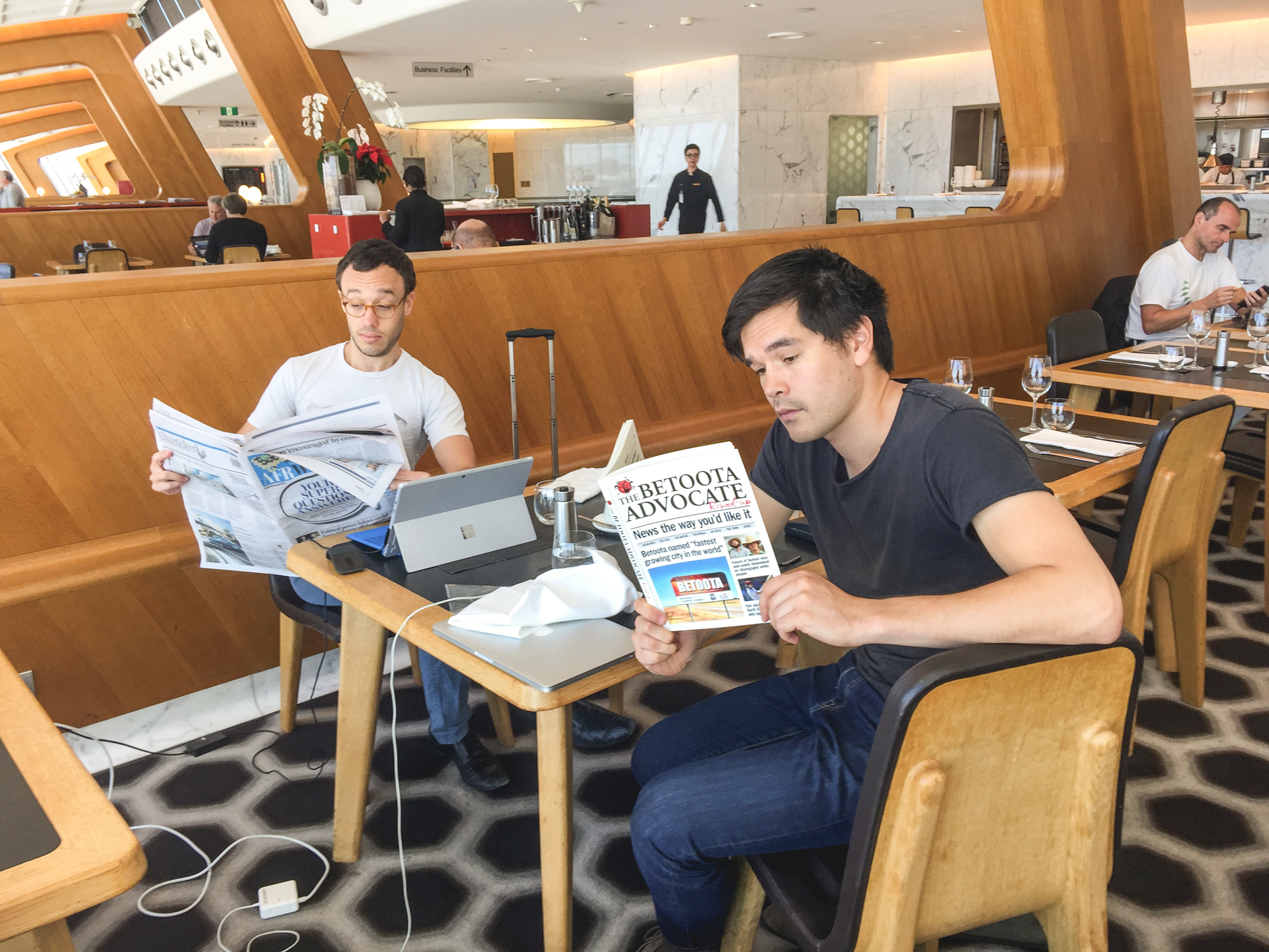Two Snappr cofounders reading newspapers at airport business lounge with Surface tablet on the table