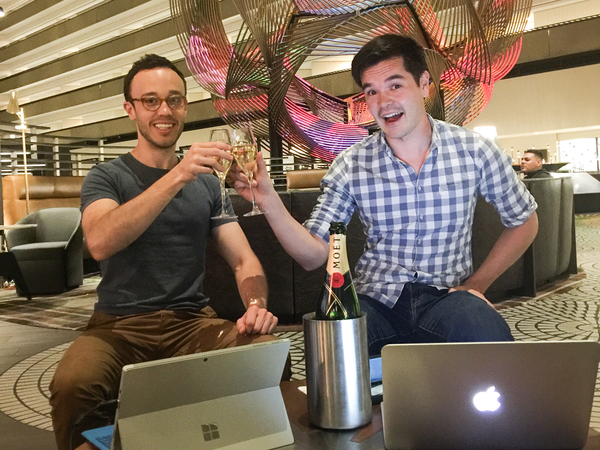 Two Snappr team members toasting with champagne flutes and Moet bottle while celebrating with laptops