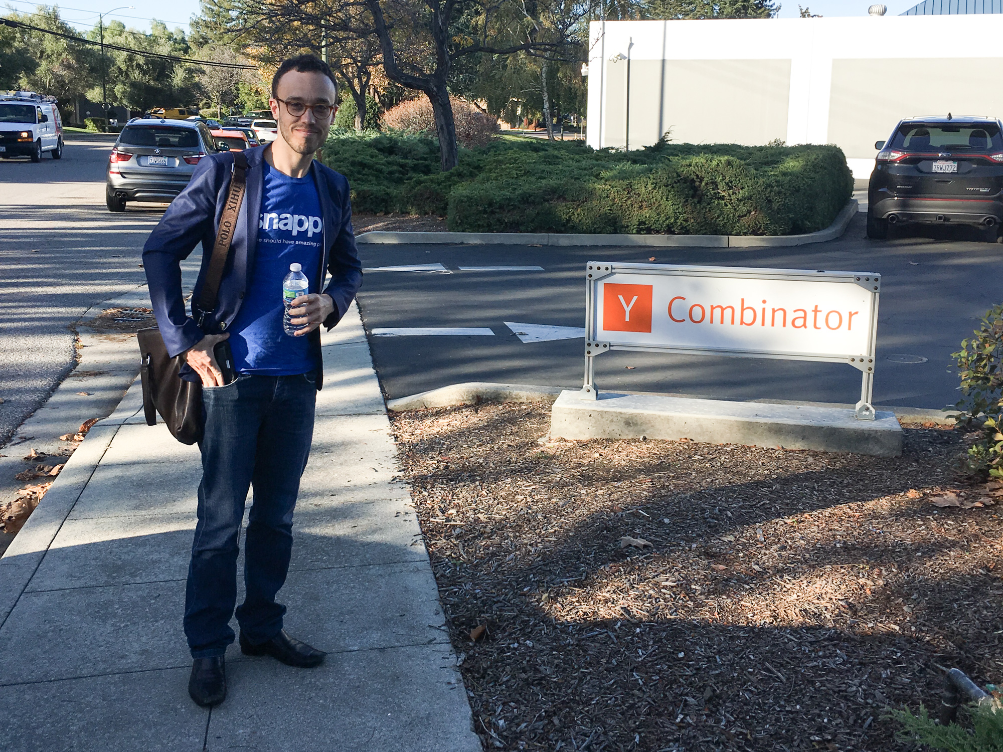 Matt Schiller in branded blue t-shirt standing next to the Y Combinator sign at headquarters