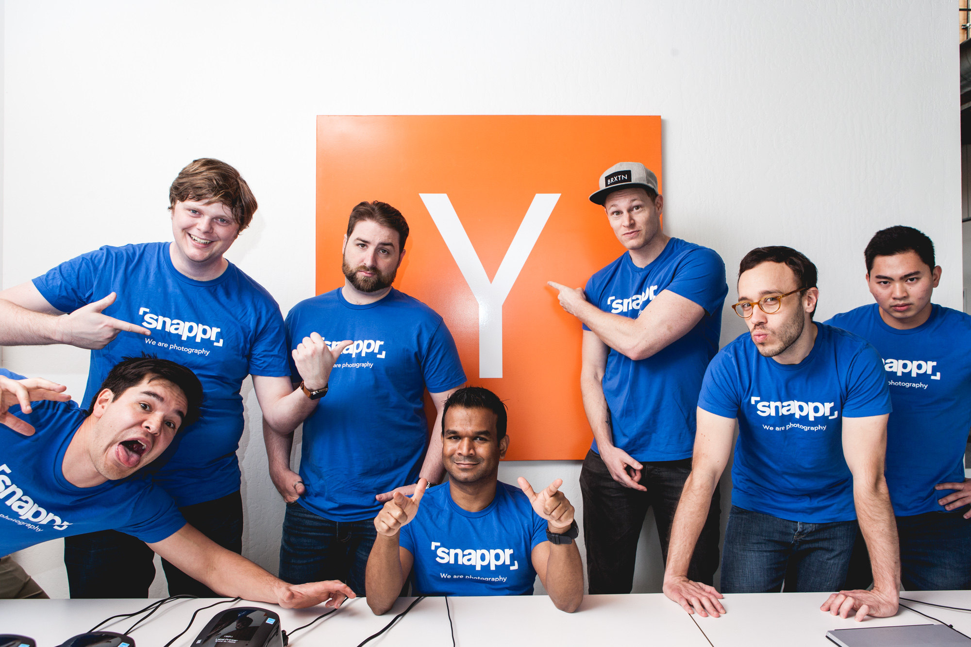 Snappr team in branded blue t-shirts posing in front of the orange Y Combinator logo for fun group photo