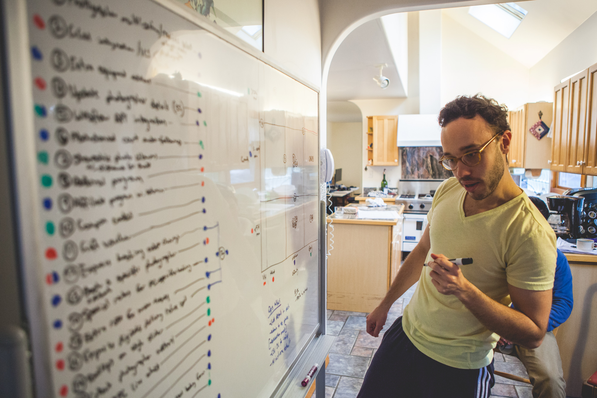 Snappr cofounder reviewing tasks whiteboard filled with handwritten goals at YC house kitchen workspace