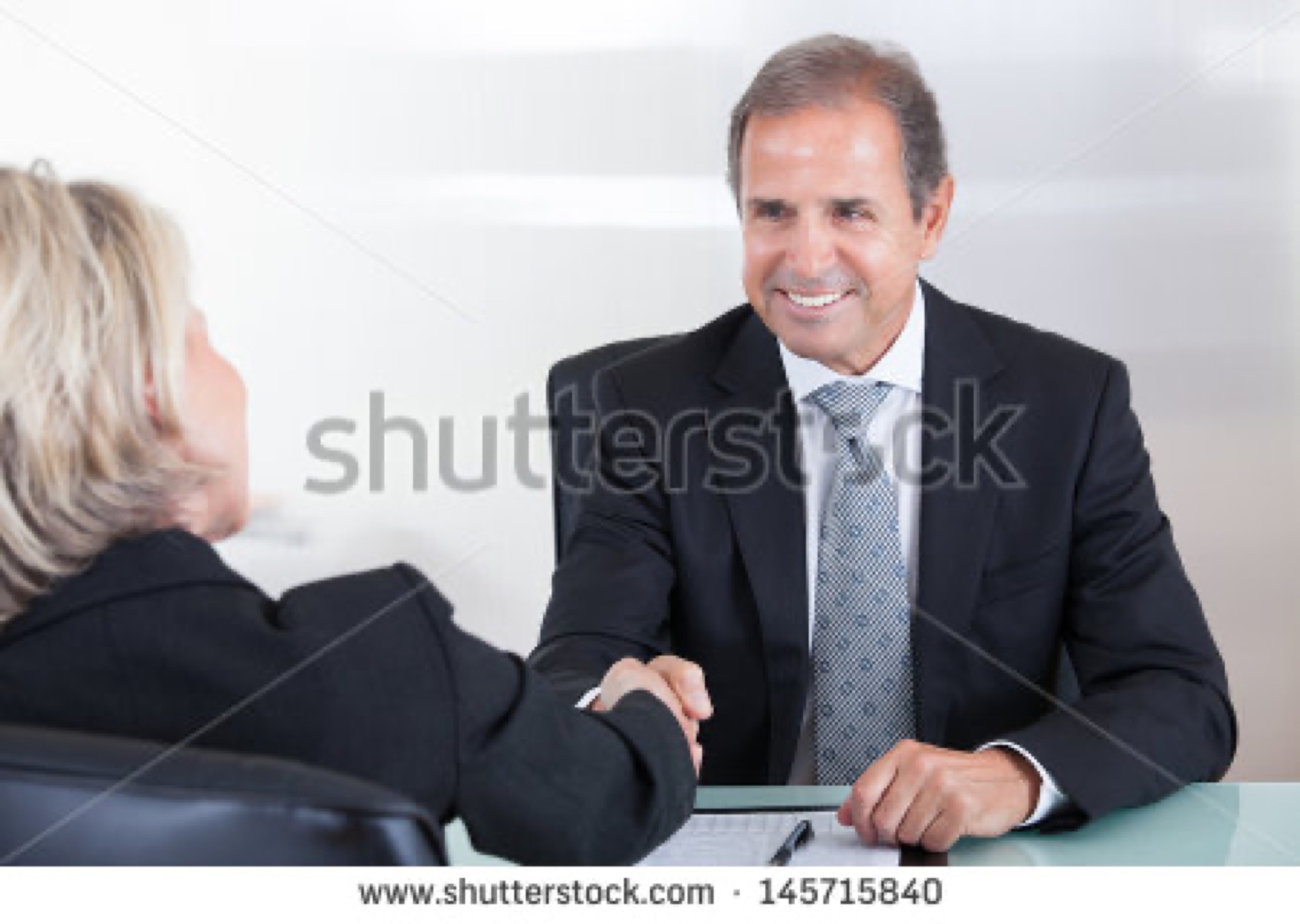 Smiling senior businessman shaking hands across a desk in an office meeting, the archetypal friendly senior business guy overused stock photo cliche