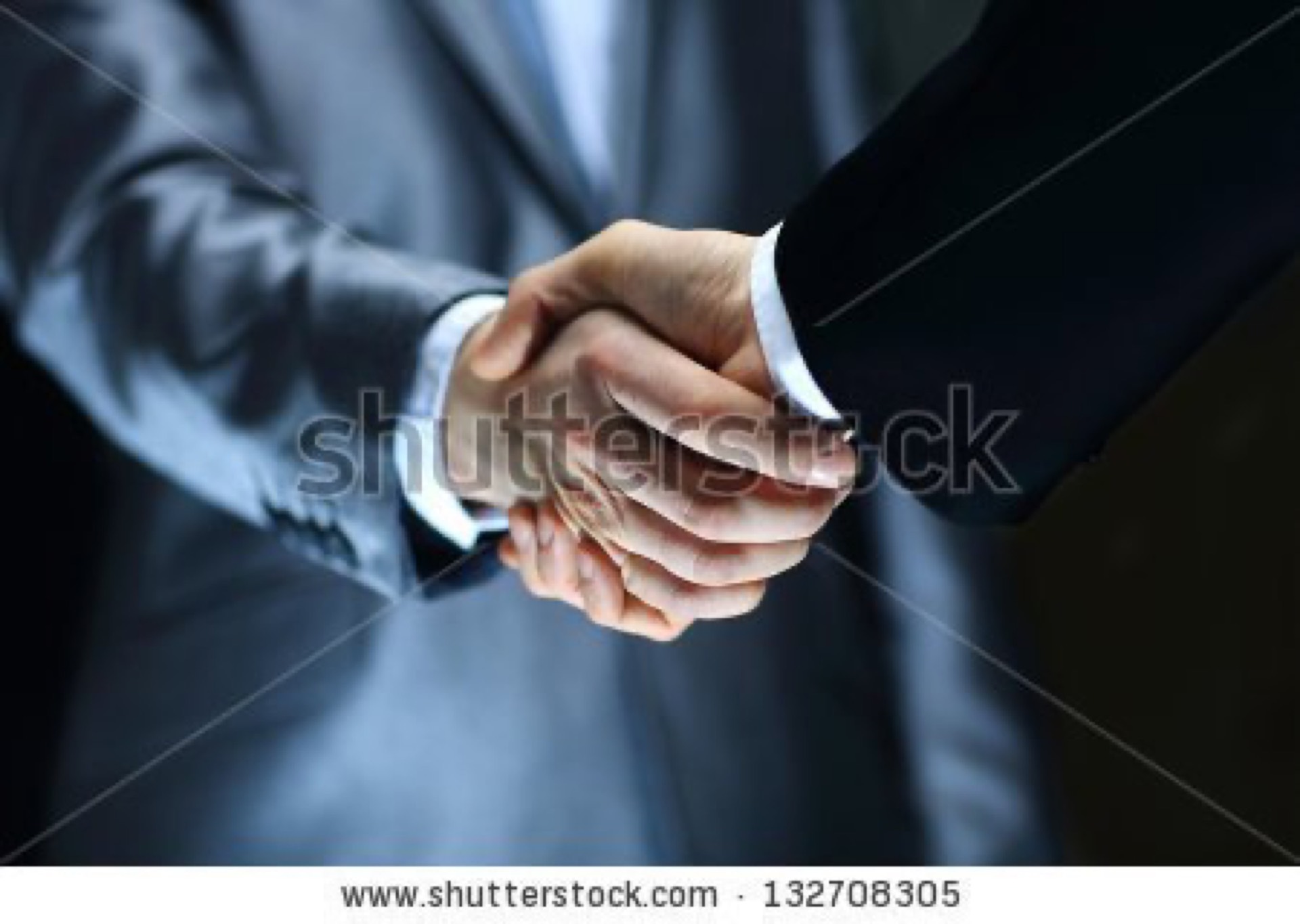 Close-up of two suited professionals shaking hands on a dark background, one of the most overused business stock photo cliches