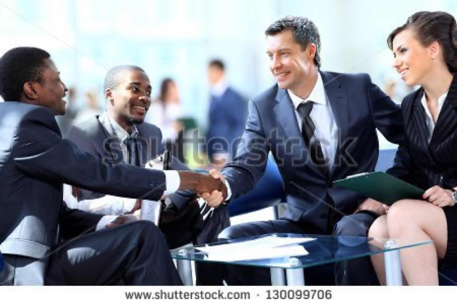Diverse group of four suited professionals shaking hands around a glass table, the quintessential overused multicultural team collaboration stock photo