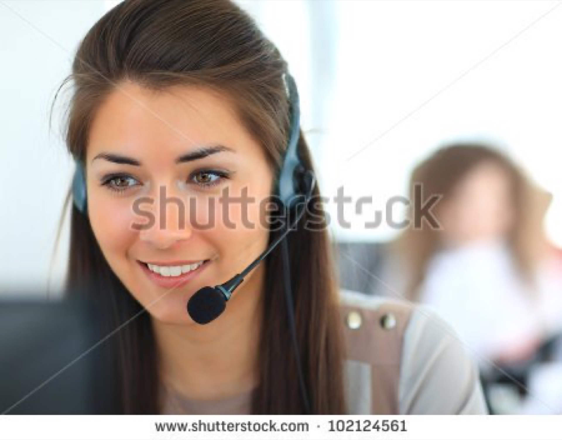 Smiling young woman wearing a call centre headset in a bright office, a frequently overused customer support stock photo cliche
