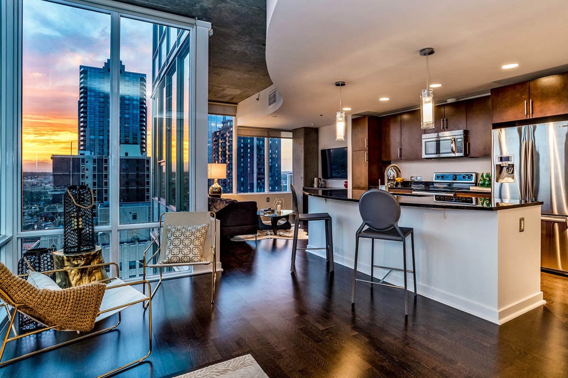 High-rise apartment kitchen and living area with dark hardwood floors and a dramatic city skyline at sunset through floor-to-ceiling windows