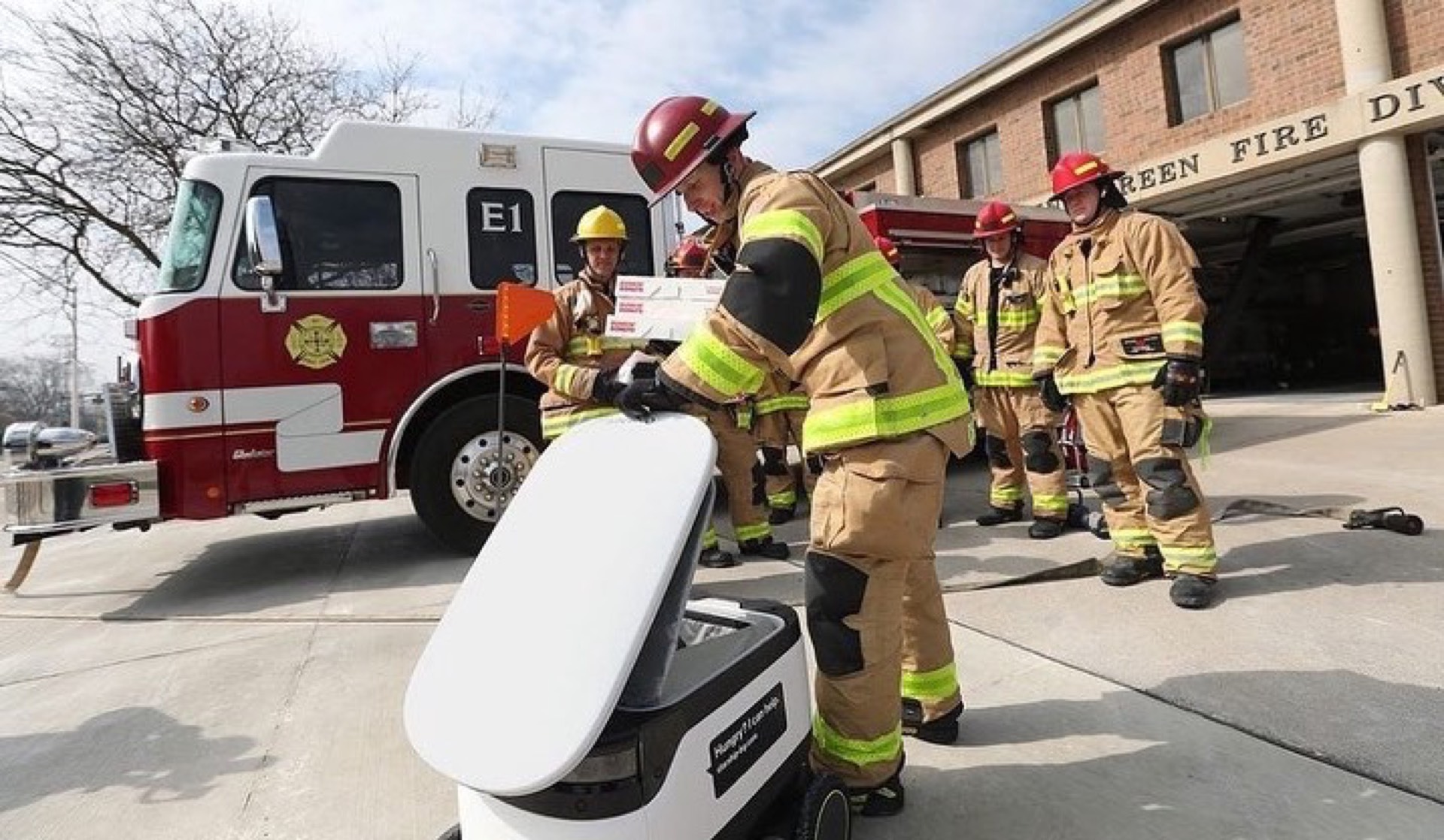 Firefighters at a fire station receiving a pizza order from a Starship autonomous delivery robot on wheels