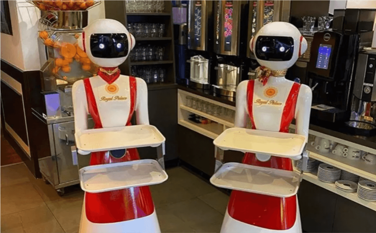 Two humanoid service robots in red-and-white uniforms holding trays at a restaurant — automated server technology in the food industry
