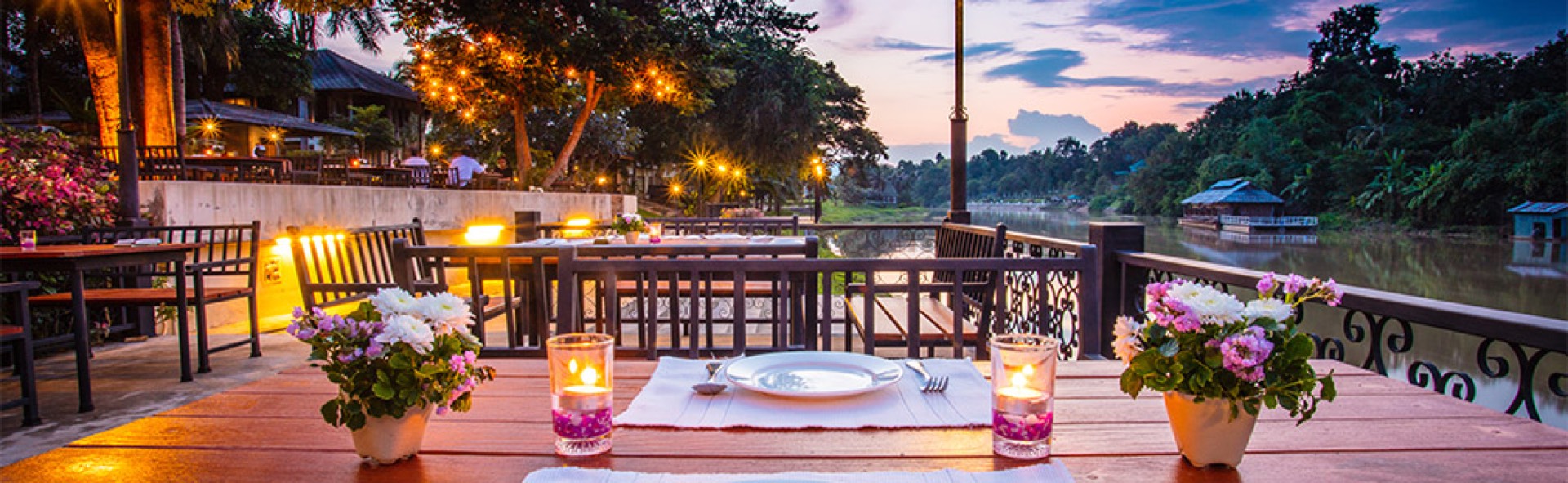 Candlelit outdoor restaurant terrace overlooking a river at dusk, ideal for al fresco dining photography