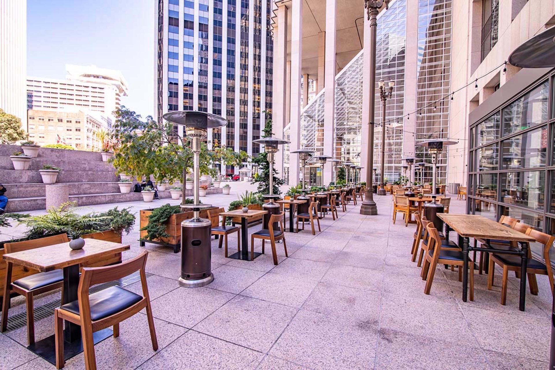 Bright outdoor patio dining area surrounded by downtown skyscrapers with wooden tables and patio heaters