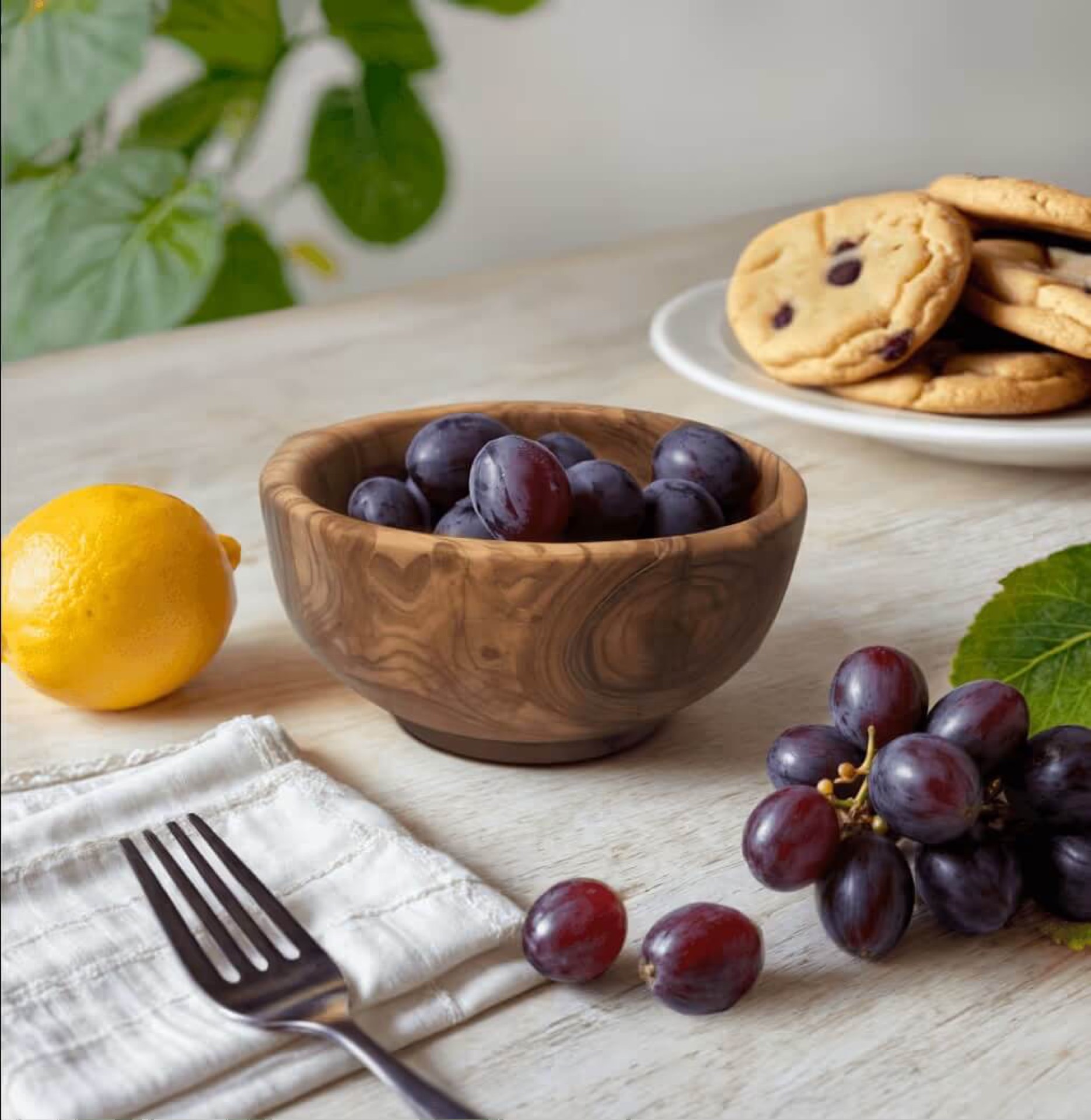 AI-generated food flatlay with grapes in a wooden bowl, lemon, and chocolate chip cookies representing generative AI photo solutions