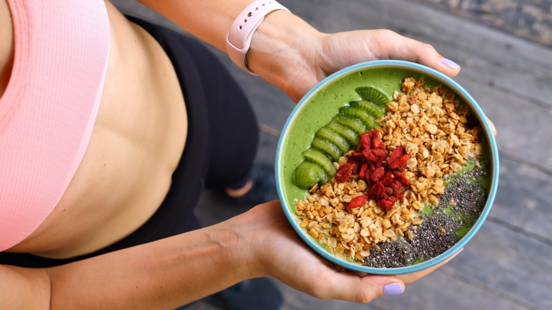 Woman in activewear holding a green smoothie bowl topped with kiwi, goji berries, and granola — high-quality food photography to drive restaurant orders