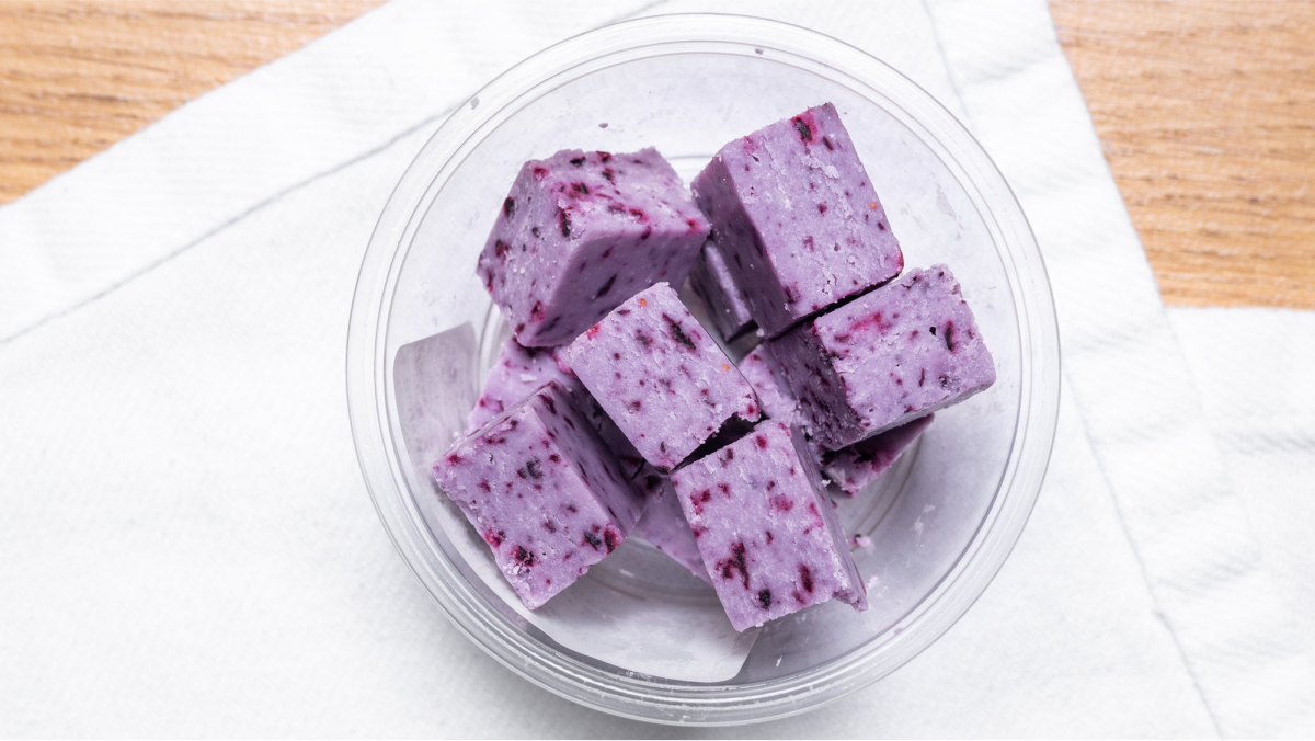 Overhead view of purple berry frozen yogurt cubes in a clear container on a white cloth — Snappr food photography May 2021
