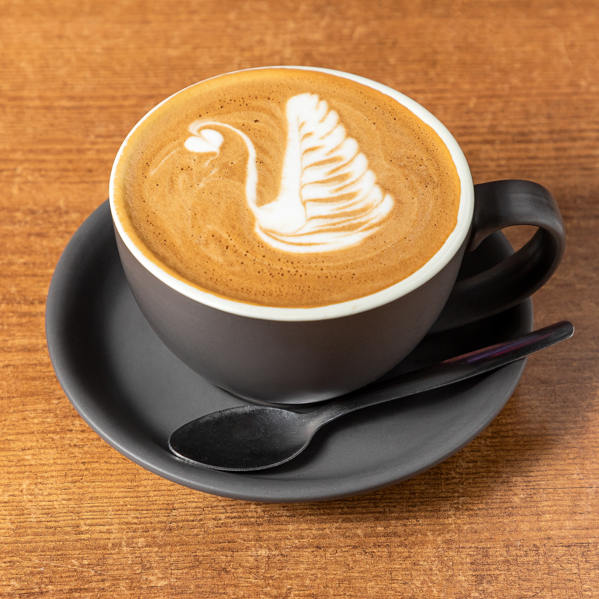 Latte art swan in a grey ceramic cup and saucer on a wooden table — Snappr food photography May 2021