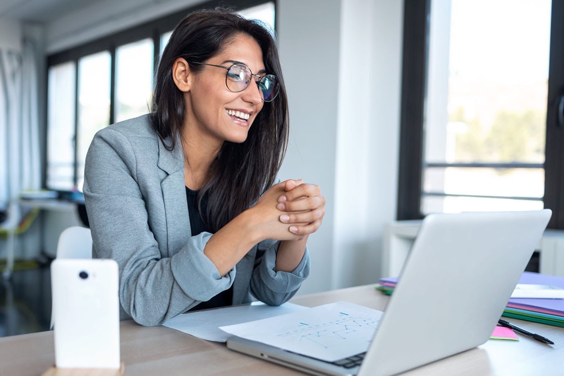 Smiling female real estate agent at a laptop in a bright office, embodying a client-focused service approach in post-Covid property marketing