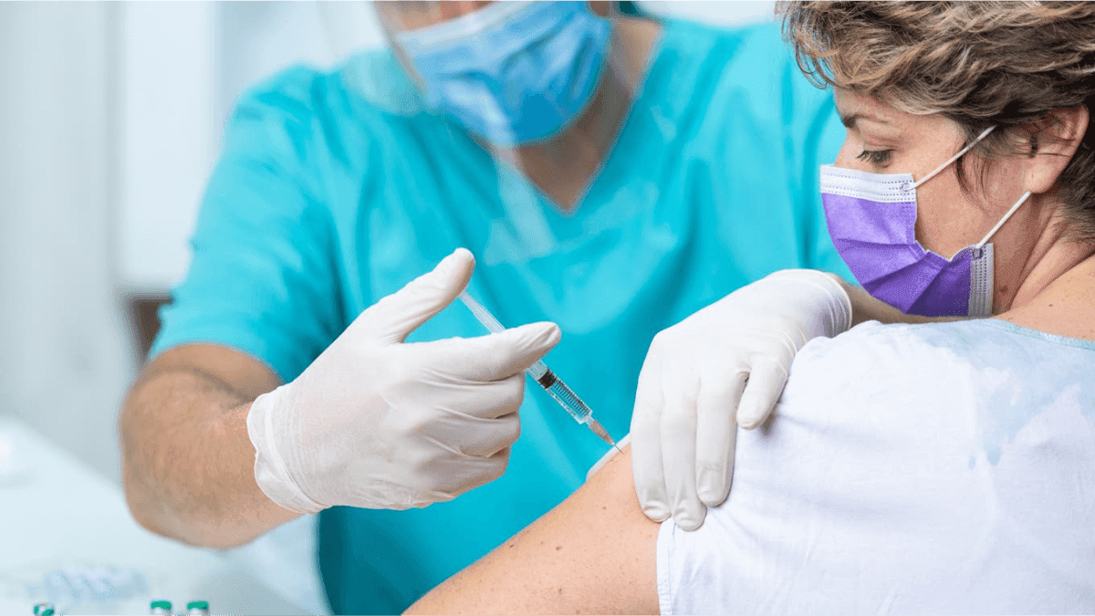 Healthcare worker administering a vaccine injection to a masked patient, representing the vaccination rollout driving the post-pandemic vacation travel boom