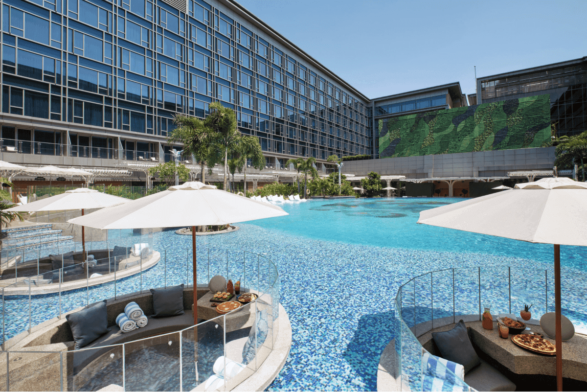 Luxury hotel outdoor pool with cabana loungers, white umbrellas, and a glass facade building, the type of professional photography that prepares hotels for the vacation boom