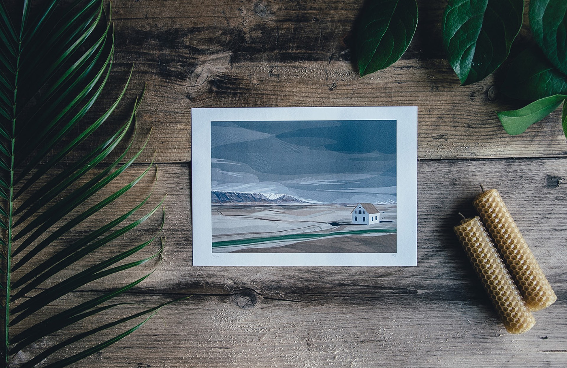 Printed landscape photograph of a lone farmhouse on a vast plain displayed on a rustic wooden surface, representing lasting memories when you print your photographs
