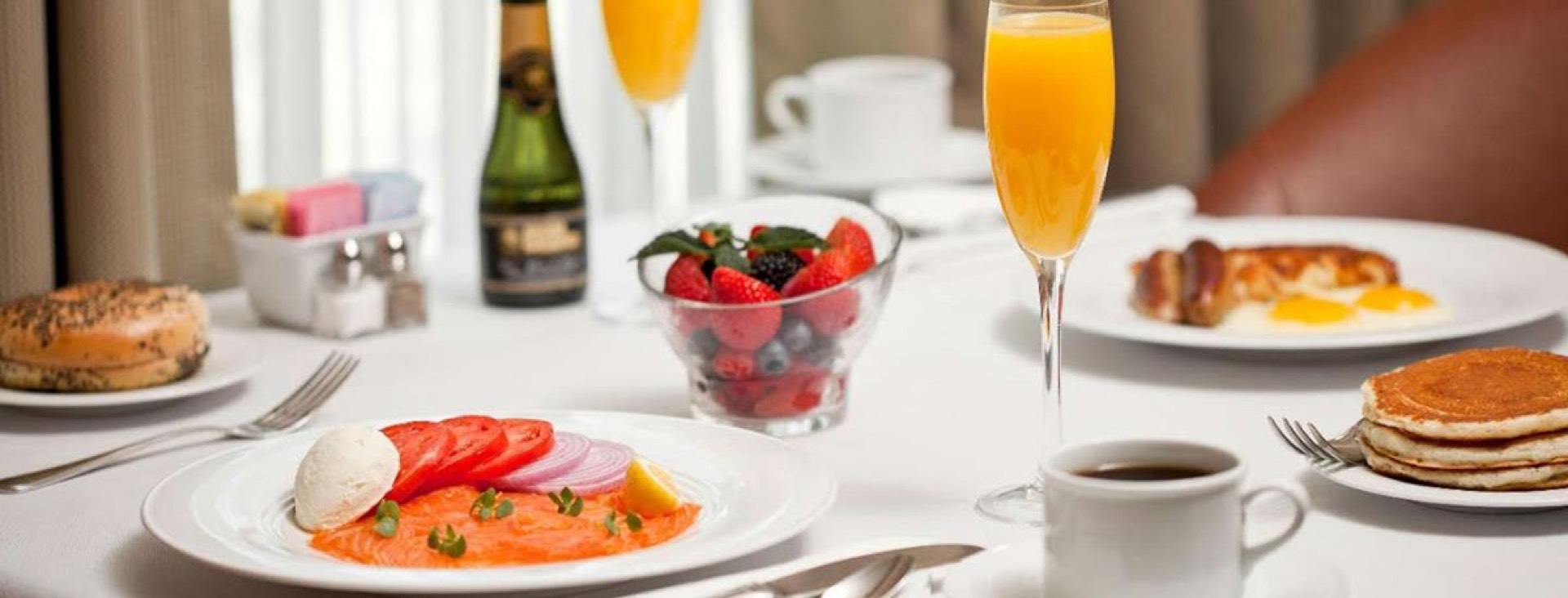 Elegant MGM Grand Las Vegas room service table set with smoked salmon, pancakes, fresh fruit, and mimosas