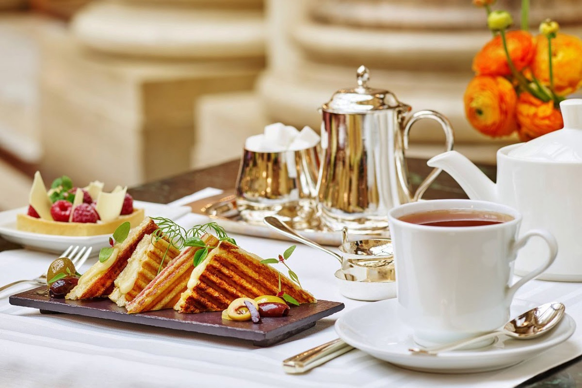 Palace Hotel San Francisco afternoon tea service with grilled panini, silver tea set, and orange floral arrangement