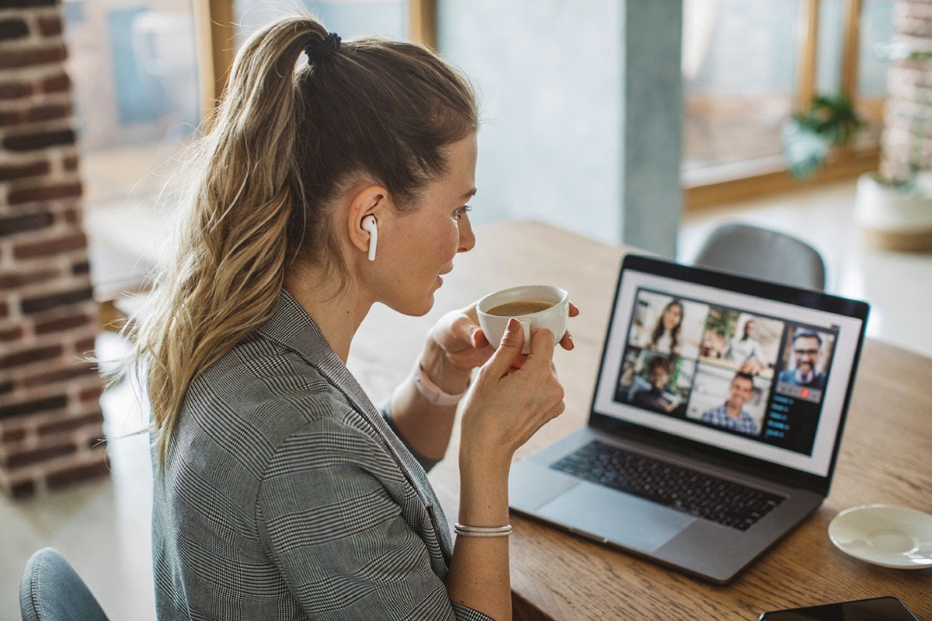 Woman holding a coffee cup joining a video call on her laptop at home — symbolizing COVID-era work-from-home dining trend shift