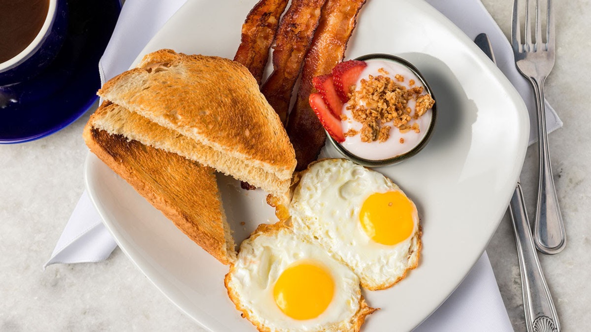 Classic American breakfast platter with fried eggs, bacon, toast, fruit and coffee — restaurant breakfast photography during COVID era