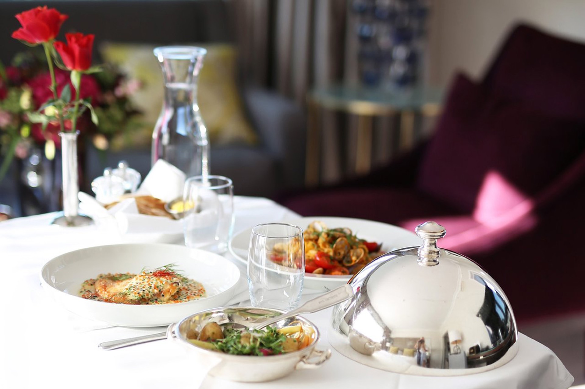 Hotel Continental Oslo in-room dining setup with silver cloche, plated main course, and red roses — flexible dining photography