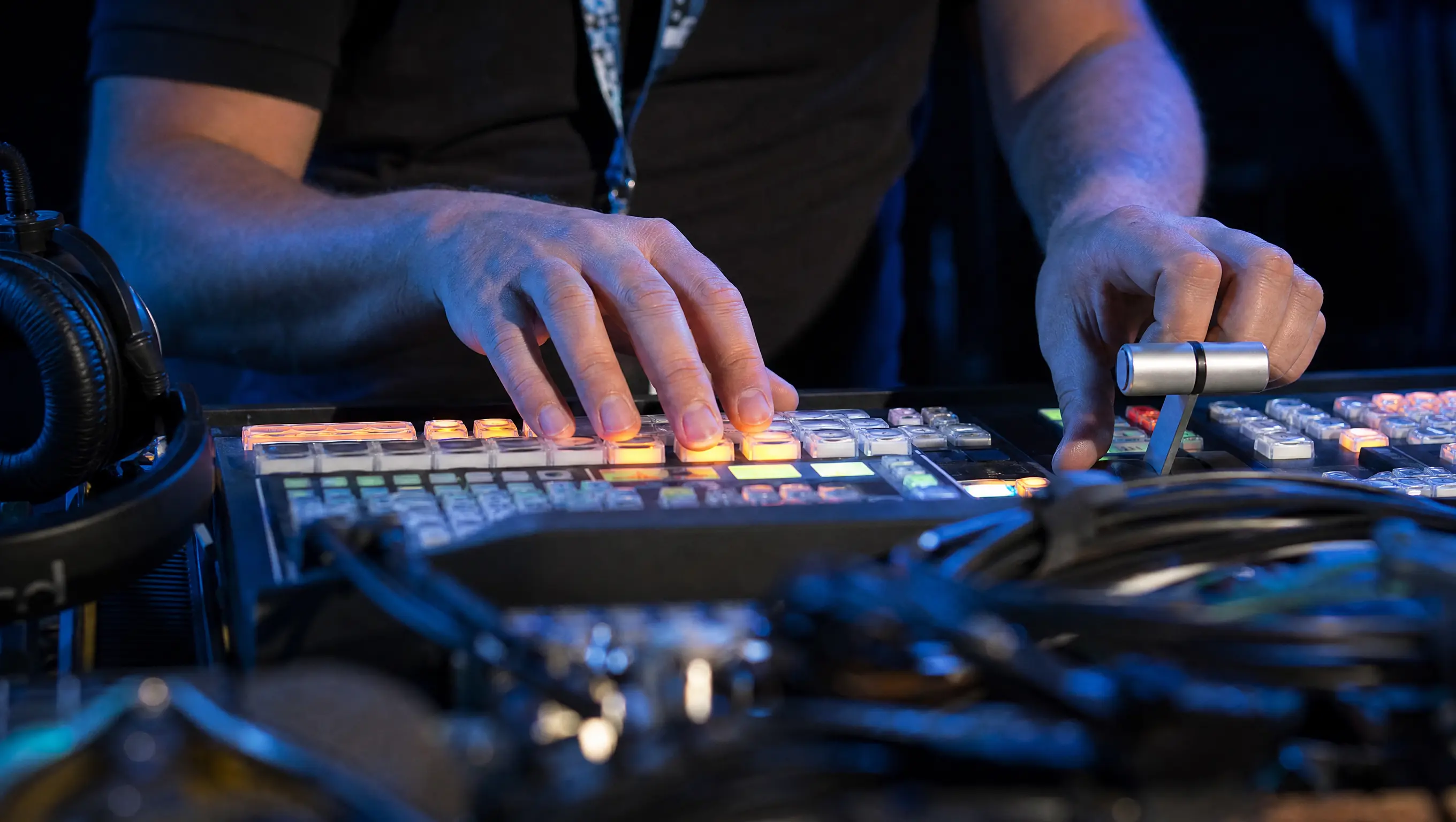 Switcher operator's hands on a video production console during a live event broadcast.