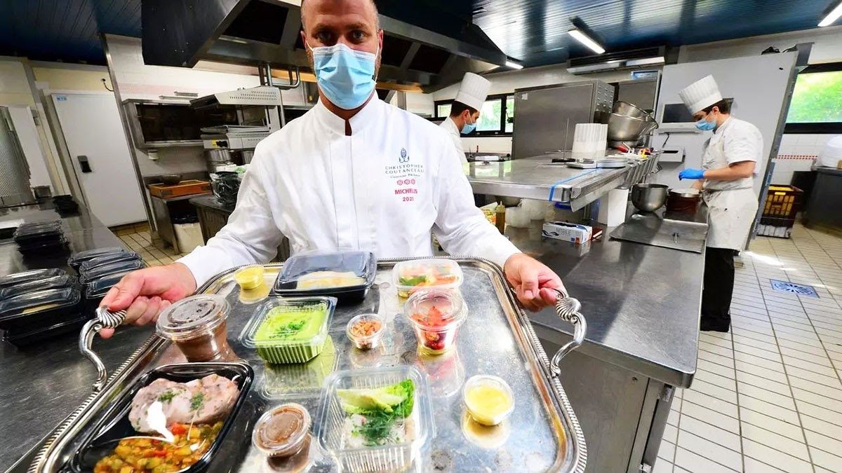 Masked chef at Coutanceau La Rochelle presenting a silver tray of individually packaged gourmet dishes prepared for contactless hotel room service
