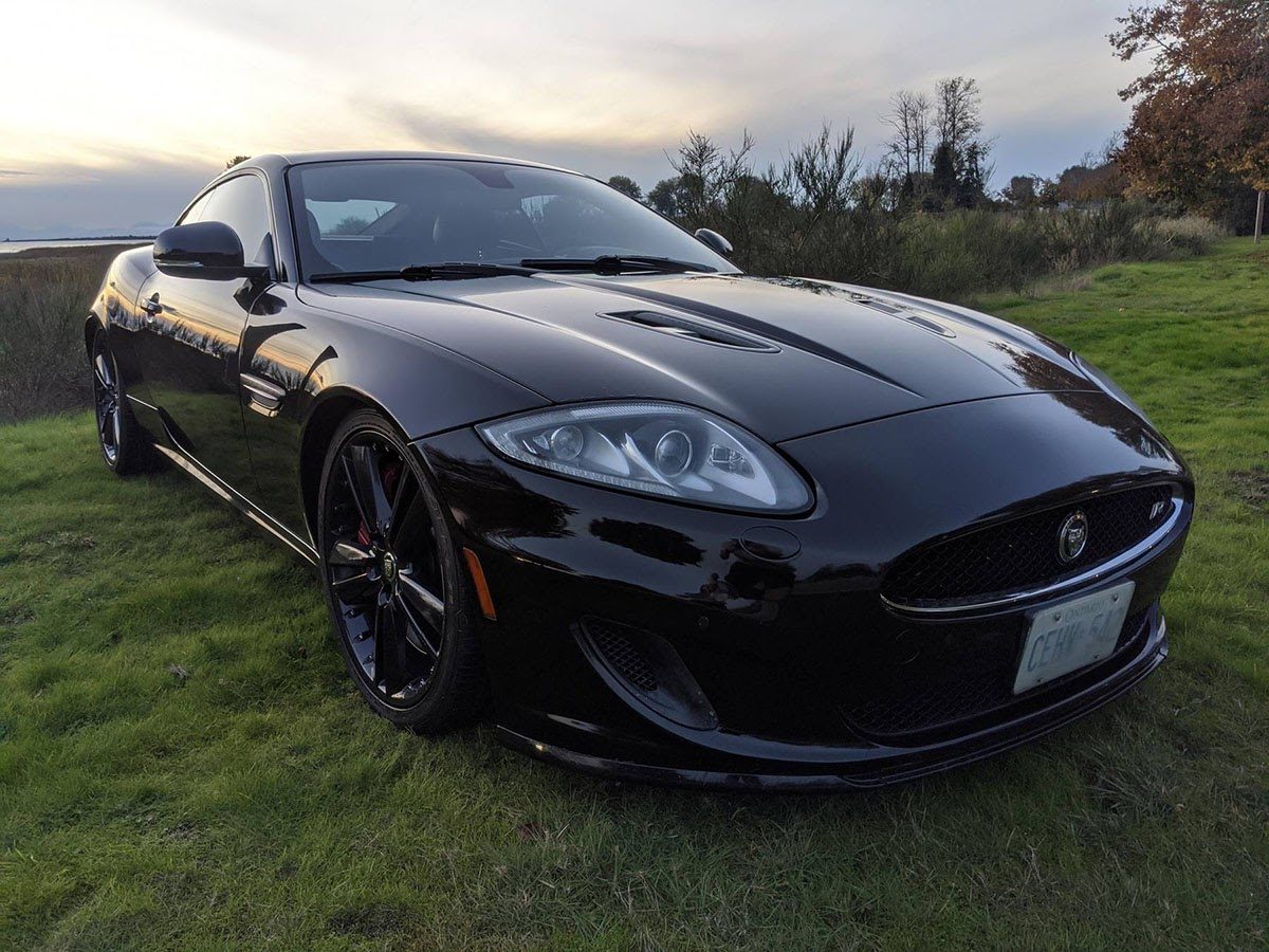 Black Jaguar XKR coupe on grass listed on Cars and Bids