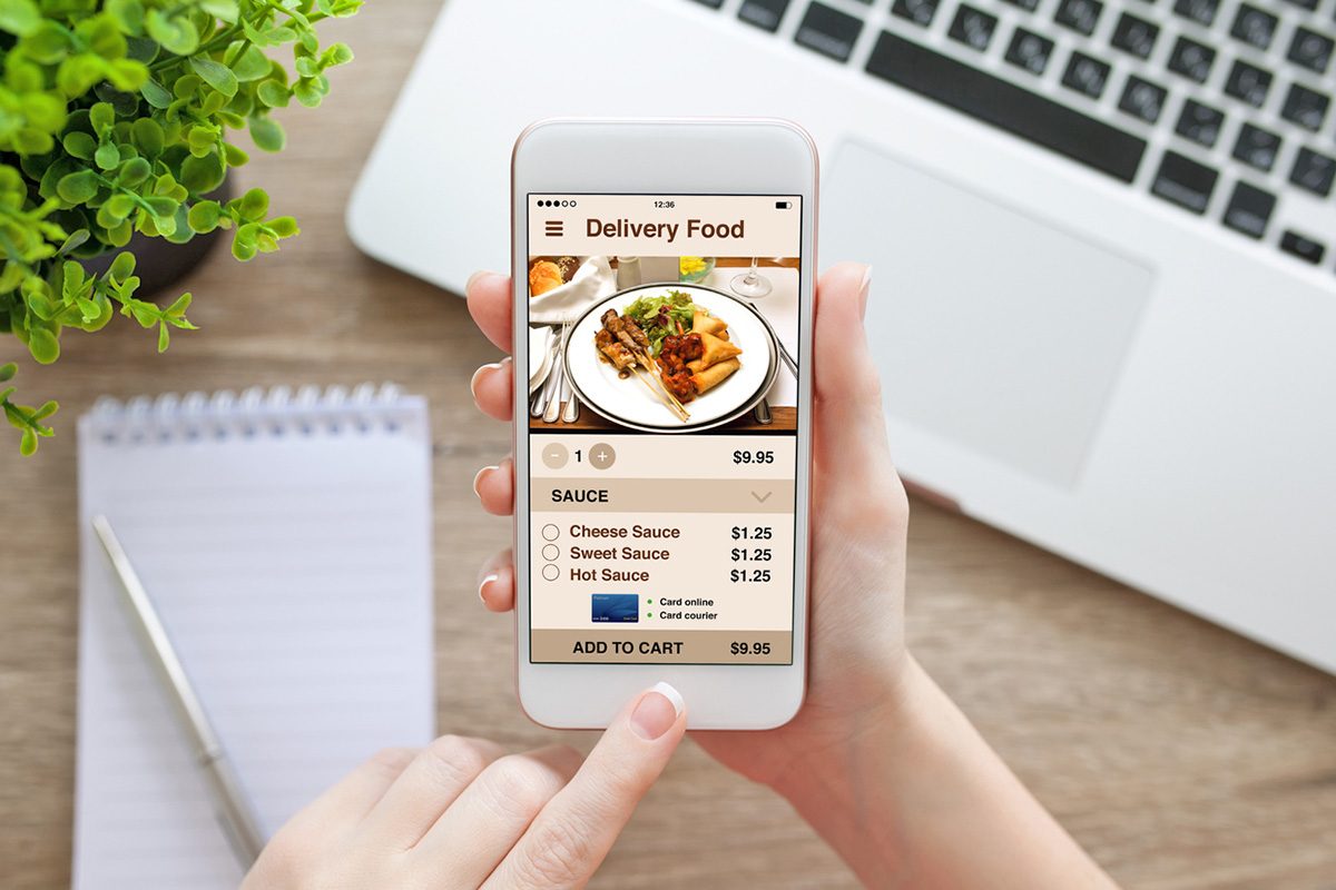 Person ordering food on a smartphone delivery app with meal options and add-to-cart button