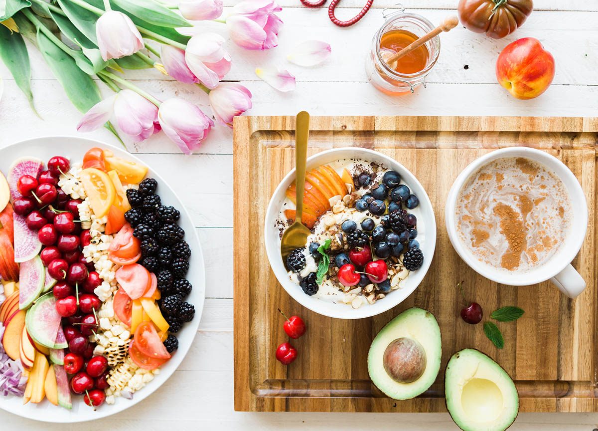 Flat-lay of a colorful healthy food spread with fresh fruit bowls, avocado, honey, and granola