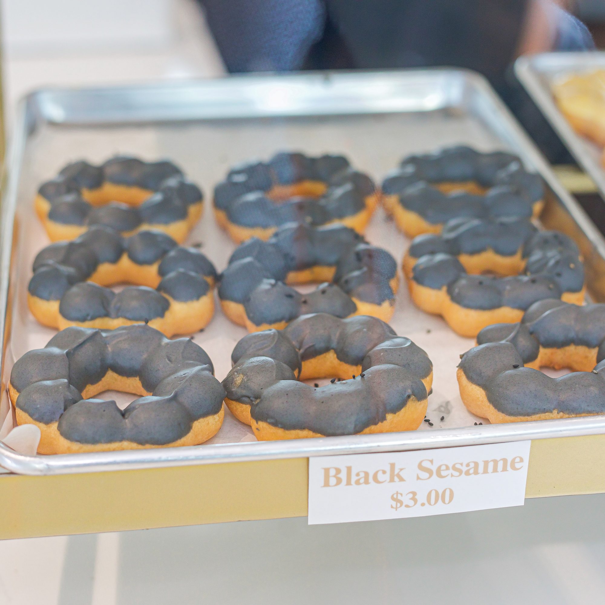 Close-up of black sesame glazed donuts on a bakery tray with a three dollar price tag