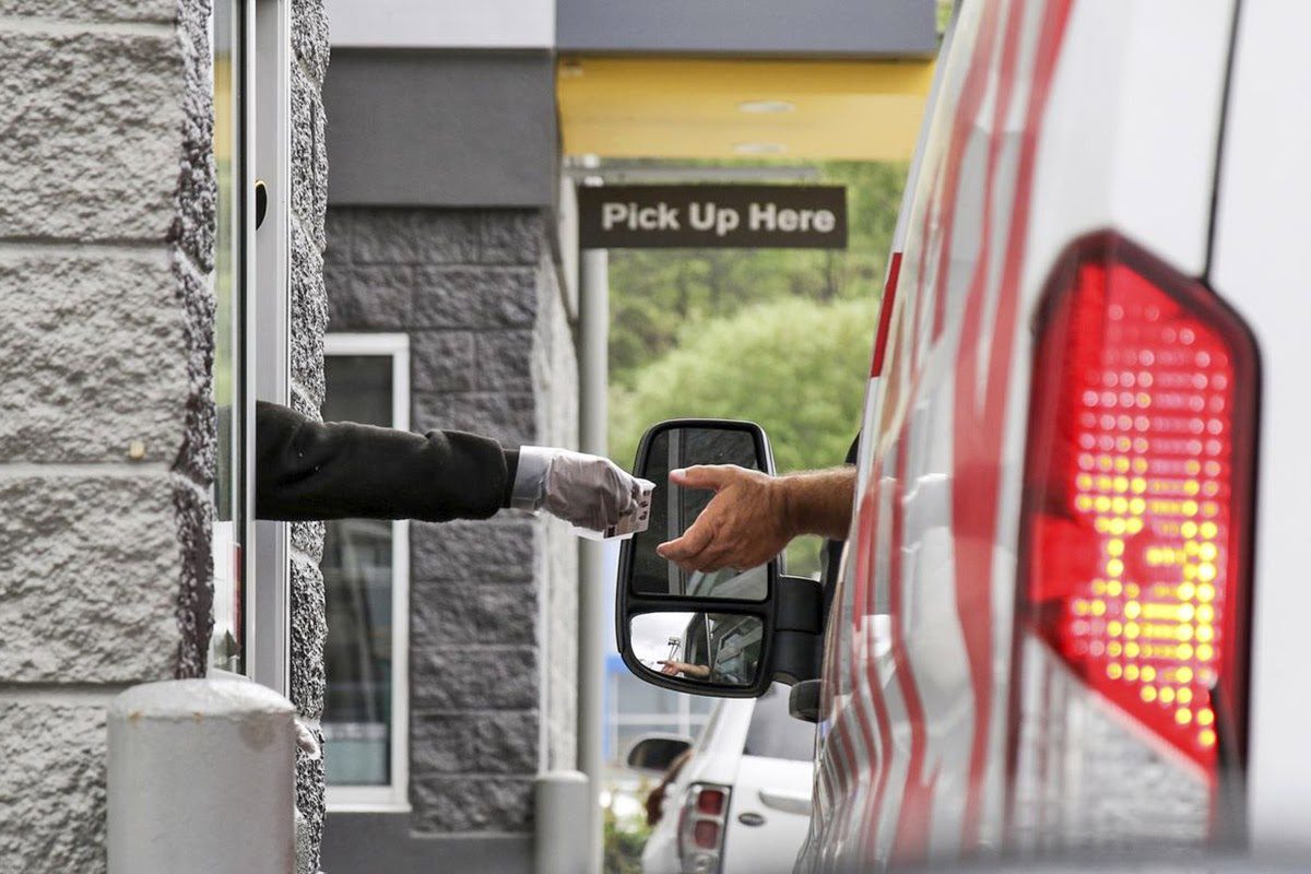 Drive-thru pickup window with gloved employee handing change to customer under a Pick Up Here sign
