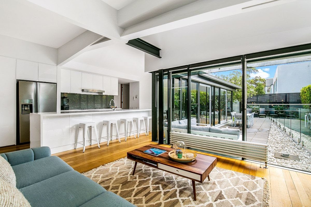 Open-plan kitchen and living room with white cabinetry, timber floors, and bifold doors opening to an outdoor terrace