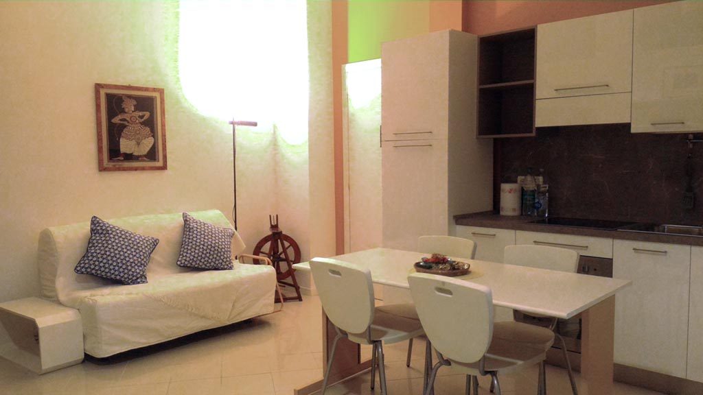 Amateur apartment photo with poor lighting and color cast showing a living room and kitchen area