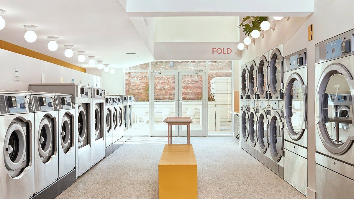 Modern laundromat with rows of commercial washing machines and a folding station in a bright, well-lit rental property amenity space