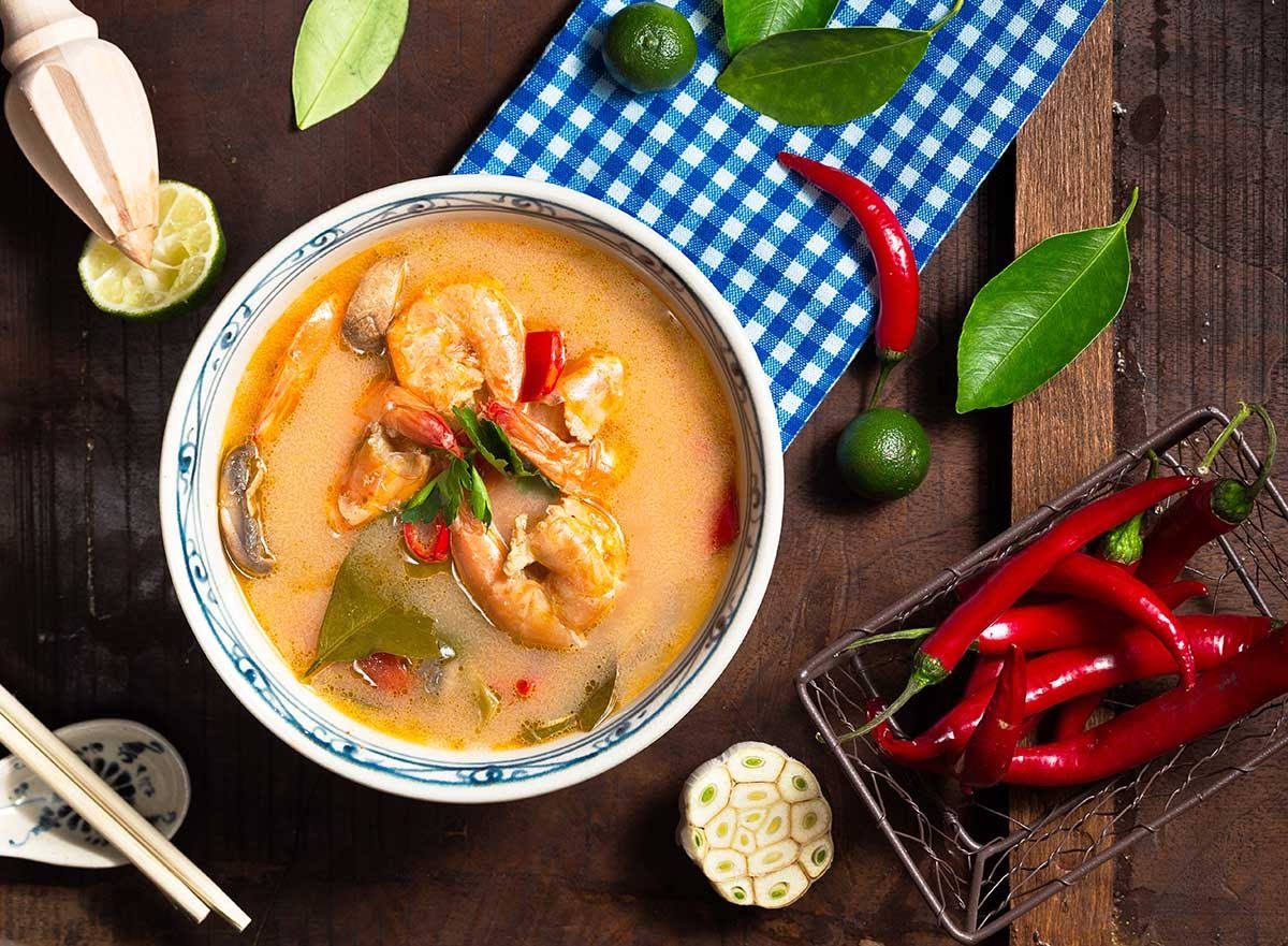 Overhead view of Thai tom yum soup with shrimp, mushrooms, and fresh red chilies on a wooden table