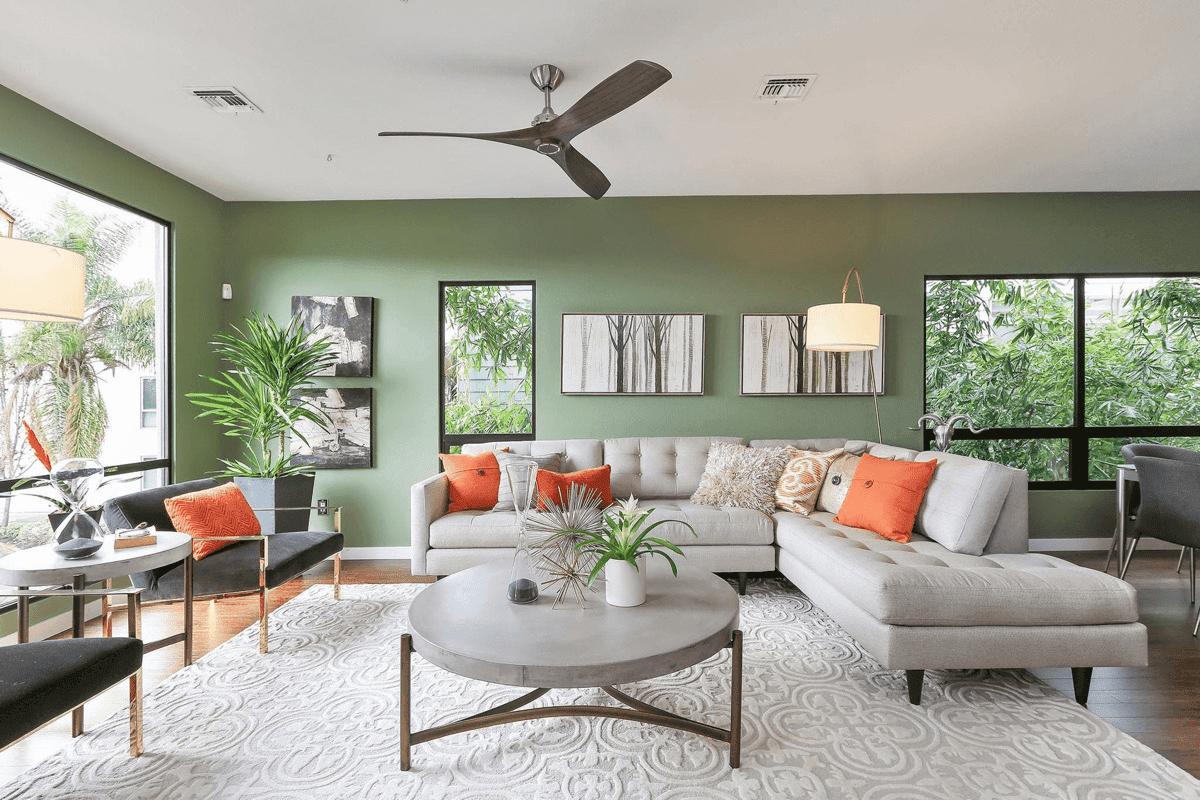 Professionally staged living room with sage green walls sectional sofa and orange accent pillows