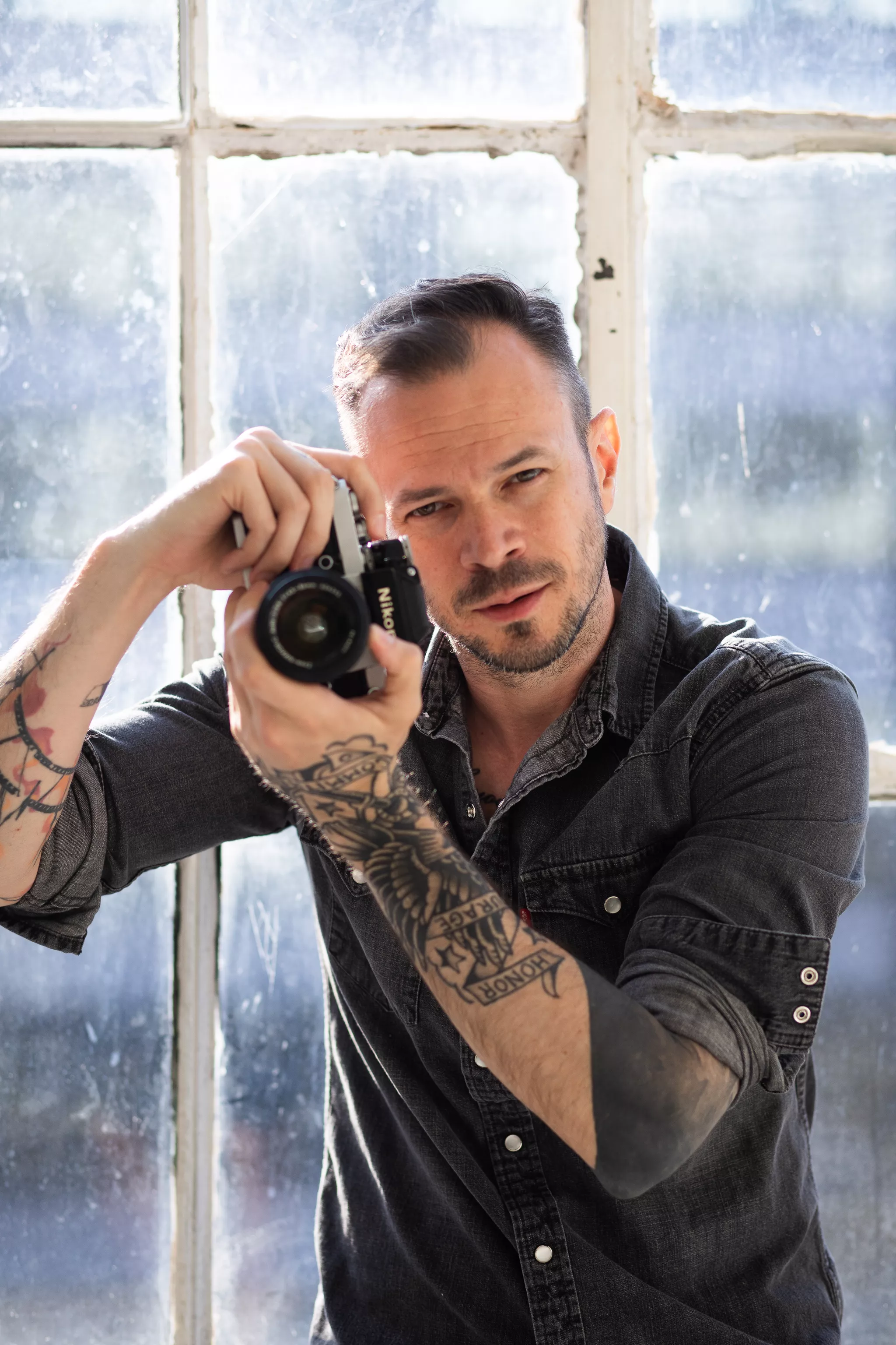 Photographer framing a shot on a Nikon camera in natural window light.