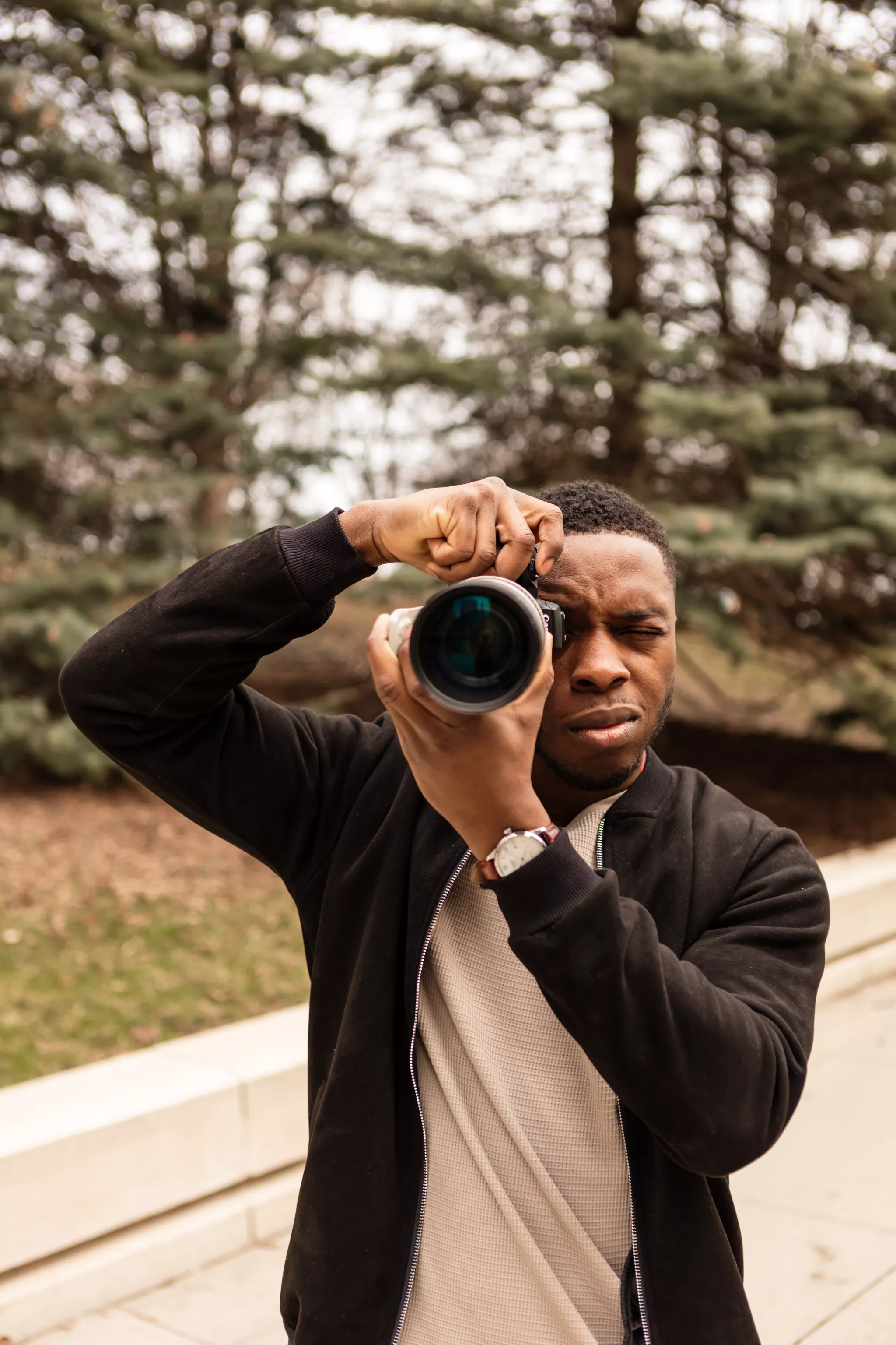 Portrait photographer framing a shot with a telephoto DSLR among park trees.