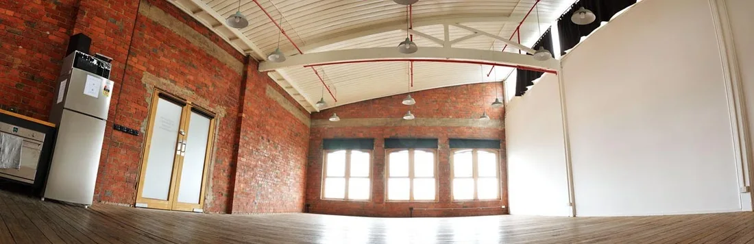 Empty industrial photography studio in Melbourne with exposed brick walls, wooden floor, arched white ceiling, and tall arched windows