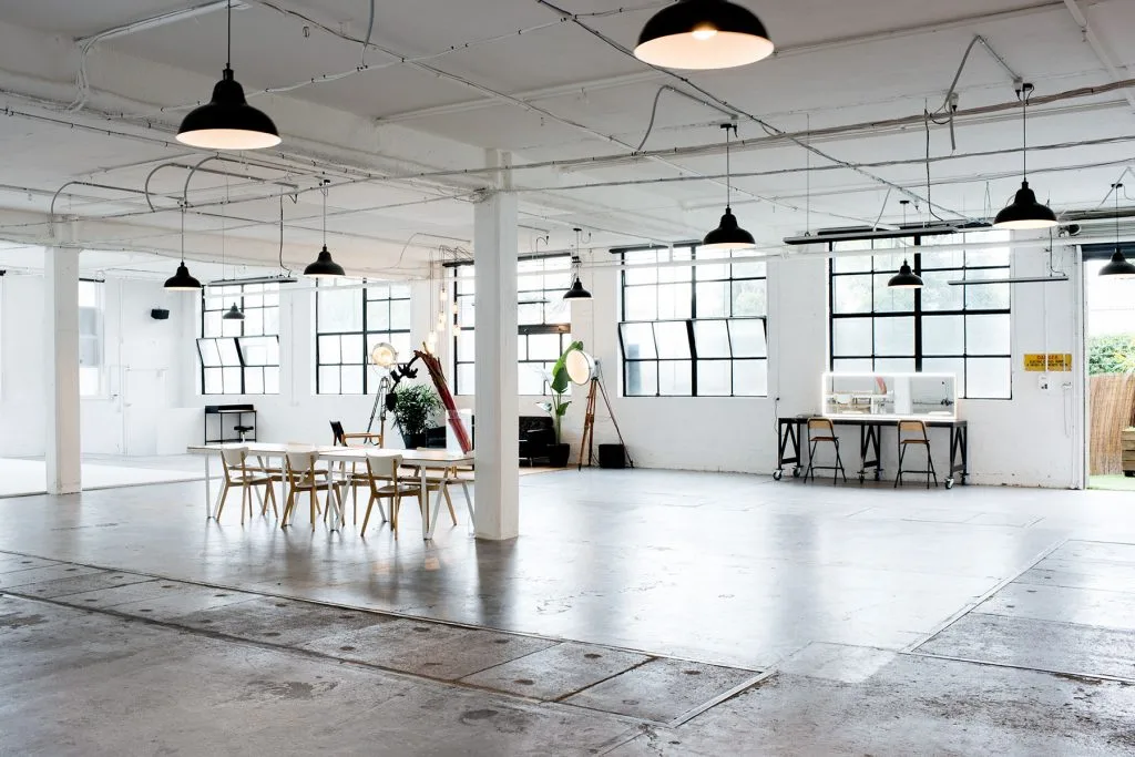 Spacious open-plan photography studio interior with industrial pendant lights, white columns, polished concrete floor, and large factory windows