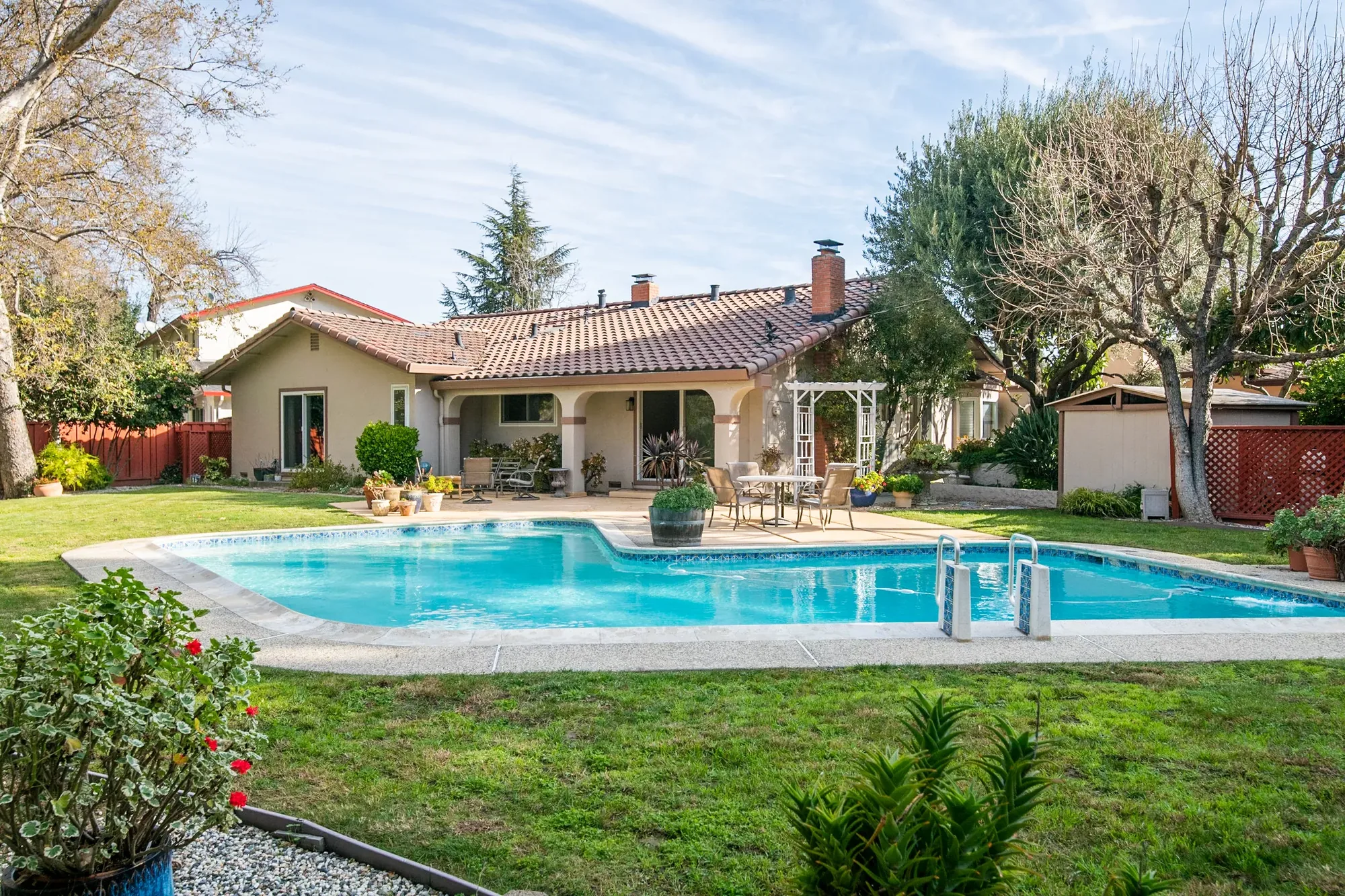 Backyard in-ground pool and patio behind a single-story tile-roof home.