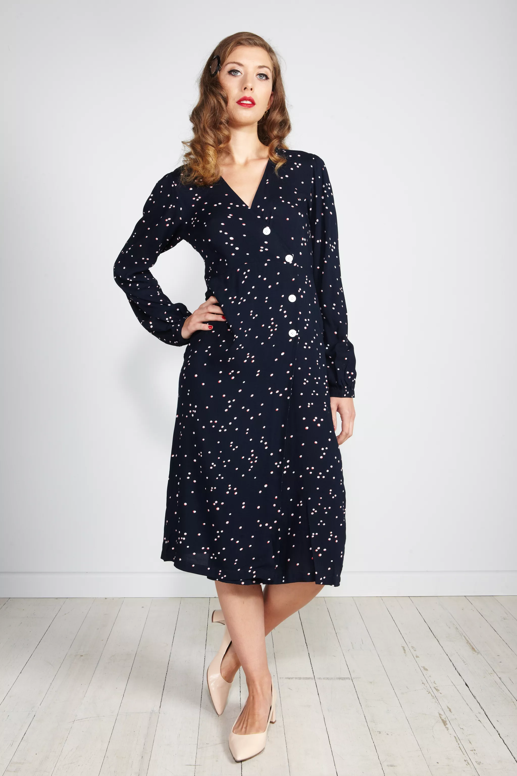 On-model apparel photography of a navy polka-dot dress on a studio backdrop.