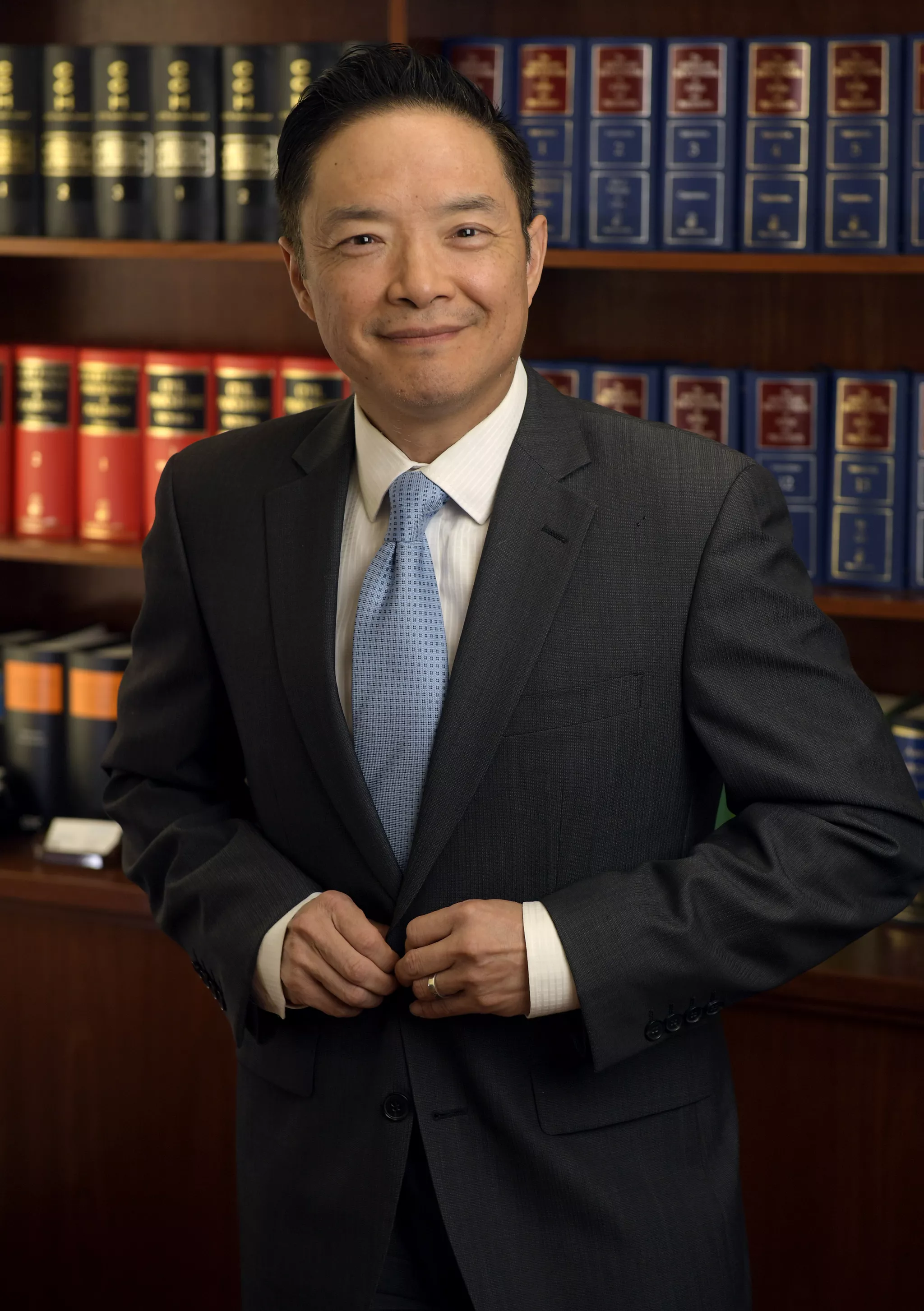 Editorial portrait of a man in a suit buttoning his jacket in a law library.