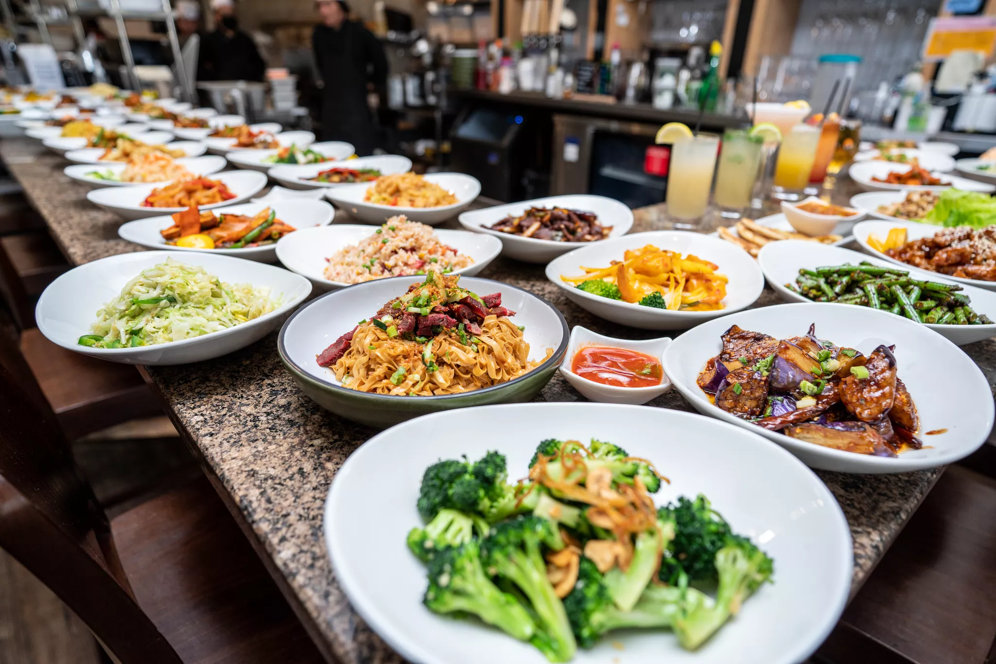Dozens of plated dishes lined up along a bar during a full restaurant menu photo shoot.